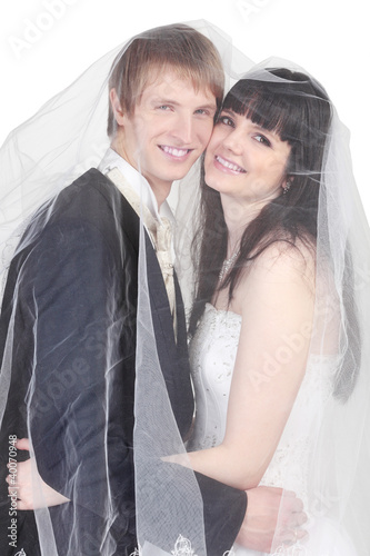 Photo: Happy young groom and bride hide under transparent veil isolated Happy young groom and bride hide under transparent veil isolated