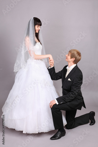 Photo: Happy groom kneels and holds beautiful bride hand in studio Happy groom kneels and holds beautiful bride hand in studio