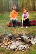 Two children sit around campfire and poke by sticks into ashes