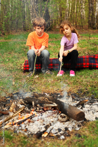 Photo: Two children sit around campfire and poke by sticks into ashes Two children sit around campfire and poke by sticks into ashes