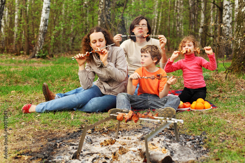 Photo: Mother, father and children eat grilled shish kebab outdoor Mother, father and children eat grilled shish kebab outdoor