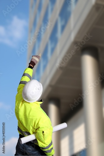 Photo: Bauarbeiter mit Planrolle deutet auf Hochhaus Bauarbeiter mit Planrolle deutet auf Hochhaus