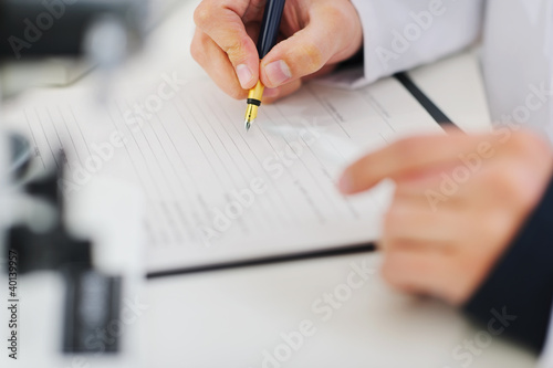 Photo: Closeup writing in document hands of medical doctor Closeup writing in document hands of medical doctor