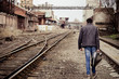 Foto: Young man with guitar case is going away among industrial ruins Young man with guitar case is going away among industrial ruins