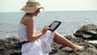 Young woman with tablet computer sitting on the rocks by the sea
