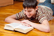 Handsome teenage boy reading the book lying on the floor