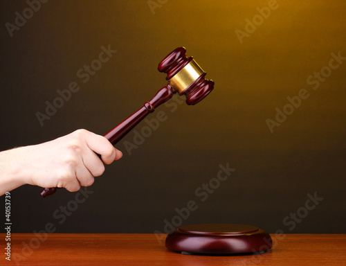 Foto: Judge's gavel in hand on brown background Judge's gavel in hand on brown background