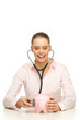 Female doctor examining piggy bank with stethoscope