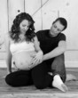 expectant couple sitting with hands on her bare belly