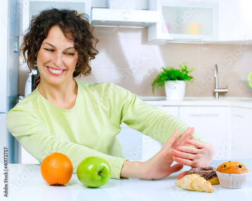 Photo: Beautiful Young Woman choosing between Fruits and Sweets Beautiful Young Woman choosing between Fruits and Sweets