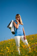 Junge blonde Frau in der Wiese mit Einkaufstaschen im Frühling Junge blonde Frau in der Wiese mit Einkaufstaschen im Frühling