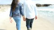 Back view of couple walking on the beach holding hands