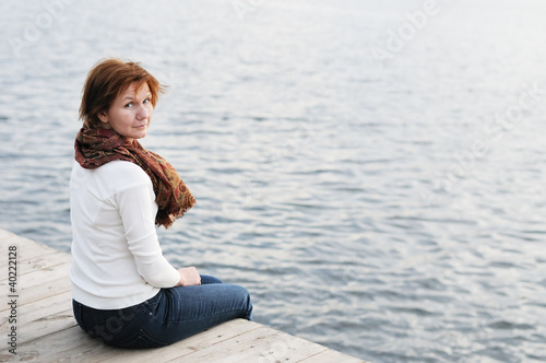 Photo: Middle age woman sitting on wood boards by the water Middle age woman sitting on wood boards by the water
