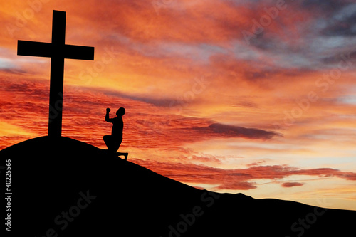 Photo: Silhouette of a man praying under the cross Silhouette of a man praying under the cross