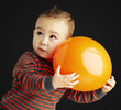 portrait of funny kid holding a big orange balloon over black ba portrait of funny kid holding a big orange balloon over black ba