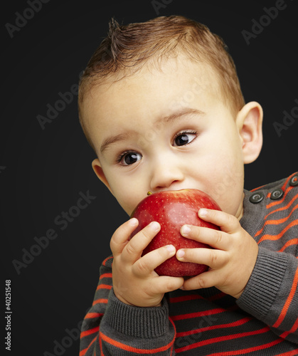 portrait of a handsome kid sucking a red apple over black backgr