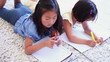 Two girls colouring while lying next to each other