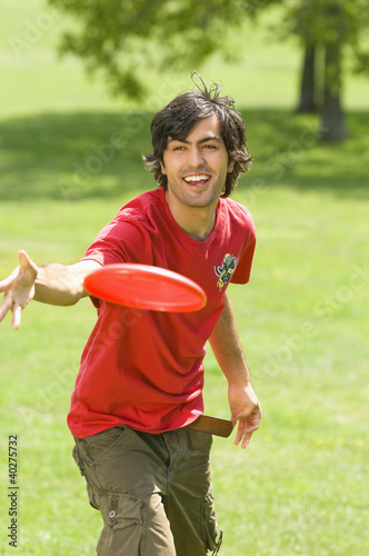 Photo: Young man playing with plastic disc on park Young man playing with plastic disc on park