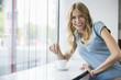 Young woman with coffee cup leaning on window sill, portrait