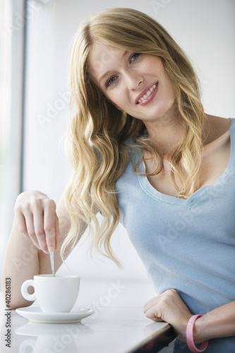 Photo: Young woman with coffee cup leaning on window sill, portrait Young woman with coffee cup leaning on window sill, portrait