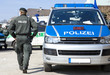 Foto: Polizist neben Einsatzwagen Polizist neben Einsatzwagen