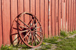 Old rustic wagon wheel beside a red barn.