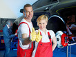 Motor mechanics and apprentice in garage show thumbs up