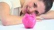 Smiling woman resting on a table with a piggy bank