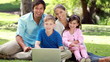 Smiling family sitting on the grass with a laptop