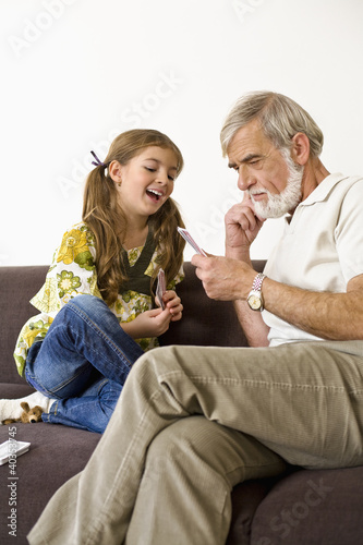 Photo: Senior man looking at cards while girl smiling Senior man looking at cards while girl smiling