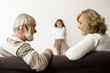 Senior man and woman sitting on sofa while girl standing by wall