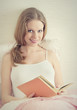 beautiful blonde girl is resting in bed, reading a book