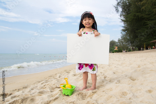 Photo: Little child girl holds a white board at beach Little child girl holds a white board at beach
