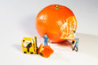 Miniatur Arbeiter schälen eine Orange
