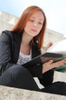 Pretty redhead student woman learning from a book, outside