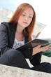 Pretty redhead student woman learning from a book, outside
