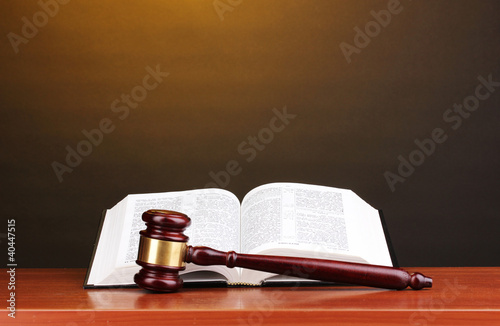 Photo: Judge's gavel and open book on wooden table on brown background Judge's gavel and open book on wooden table on brown background