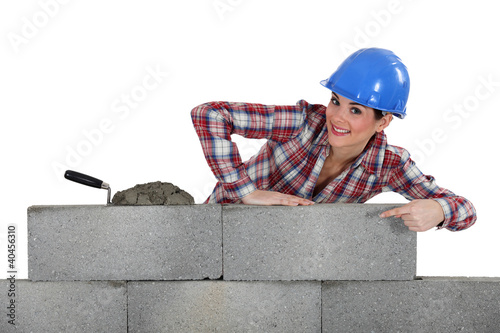 Photo: portrait of young female bricklayer pointing at concrete wall portrait of young female bricklayer pointing at concrete wall