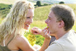 A blonde hair woman feeding her boyfriend grape.