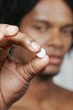 A african american man showing a pill to the camera.
