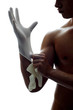 A shirtless man putting on gloves.