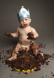 A baby with party hat playing with his birthday cake.