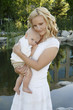 A woman carrying as baby by the pond.