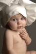A baby with chef hat looking at the camera.