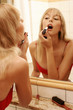 A lady in red bra applying red lipstick.