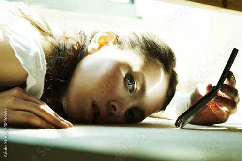 Foto: A woman lying on the bed holding a handphone. A woman lying on the bed holding a handphone.