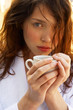 A woman in white bathrobe holding a cup of coffee.