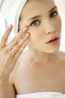 A woman with her hair and body wrapped up in towel applying undereye cream.
