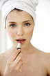 A woman with her hair and body wrapped up in towel applying lipstick.