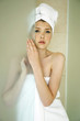 A woman with her hair and body wrapped up in towel hiding behind the shower door.